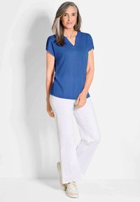 Blauw kortemouwen top met een v-halsontwerp, gecombineerd met witte flared broeken. De top heeft een gladde textuur en een ontspannen pasvorm.