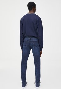 Marinblå sweatshirt med långa ärmar och avslappnad passform, i kombination med mörkblå jeans av denim med krökta bakfickor och smal form.
