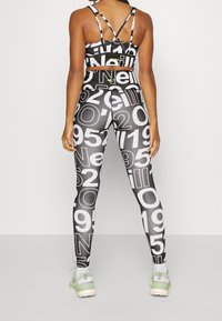 Svart och vit sport-bh med ett korsat remdesign, matchad med högmidjade leggings med stora siffror. Texturerade tygdetaljer.