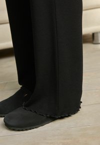 Sorte bredbenede bukser lavet af blødt stof, med en scallop-kant og parret med sorte slip-on sko med en struktureret sål.
