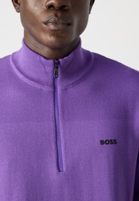 Vijolični pulover s četrt zadrgo, narejen iz mehkega pletenega materiala, z rebrastim ovratnikom in majhnim črnim logotipom "BOSS" na prsih.