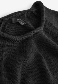 Suéter de punto negro con cuello redondo y patrones texturizados. La etiqueta dice "NEXT", talla S, fabricado en Inglaterra. Tejido suave.