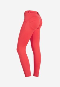 Leggings rossi aderenti realizzati in materiale elastico, con vita alta, cuciture curve e dettagli con tasche sul retro.