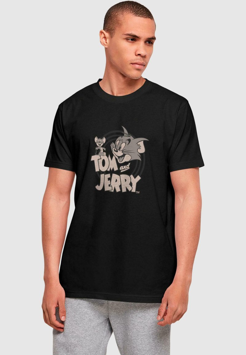 Mustvalge puuvillane T-särk, millel on vintage-stiilis halltoonides graafika Tomist ja Jerryst, allpool tegelaskujusid on julge tekst "Tom ja Jerry".