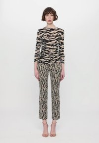 Long-sleeve sheer top in beige with black abstract stripes, paired with fitted beige patterned trousers. Soft fabric, sleek design.
