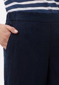 Pantalon en lin bleu marine avec une coupe décontractée, des poches latérales et une texture lisse, idéal pour une tenue décontractée.