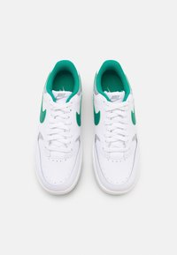 Vita Nike-sneakers med gröna logotyper och inredningar, snörda, sedda ovanifrån på en enkel vit bakgrund.