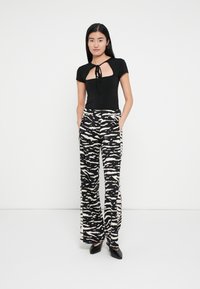 Haut noir moulant avec une découpe frontale et un détail noué, associé à un pantalon large taille haute avec un motif zèbre noir et beige.