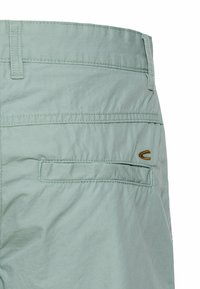 Hellgrüne Shorts aus leichtem Material mit einer Gesäßtasche, Kontrastnähten und einem kleinen braunen Logoakzent.