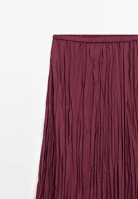 Jupe plissée bordeaux avec une taille élastique, fabriquée en tissu léger, présentant une surface texturée et des plis verticaux.