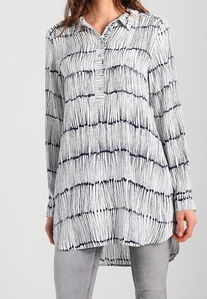 Koszula na długi rękaw zapinana na guziki, w białym i granatowym kolorze z paskowym wzorem. Posiada kołnierzyk, zaszewkę z przodu oraz wydłużony tył.