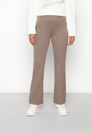 Bruine flared broeken van zachte stof, met een gladde textuur en een elastische tailleband, gecombineerd met witte sneakers en een lichte top.