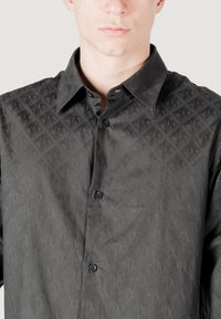 Camicia nera a fantasia con texture a rombo, colletto classico e bottoni frontali. Il tessuto appare liscio con una leggera lucentezza.