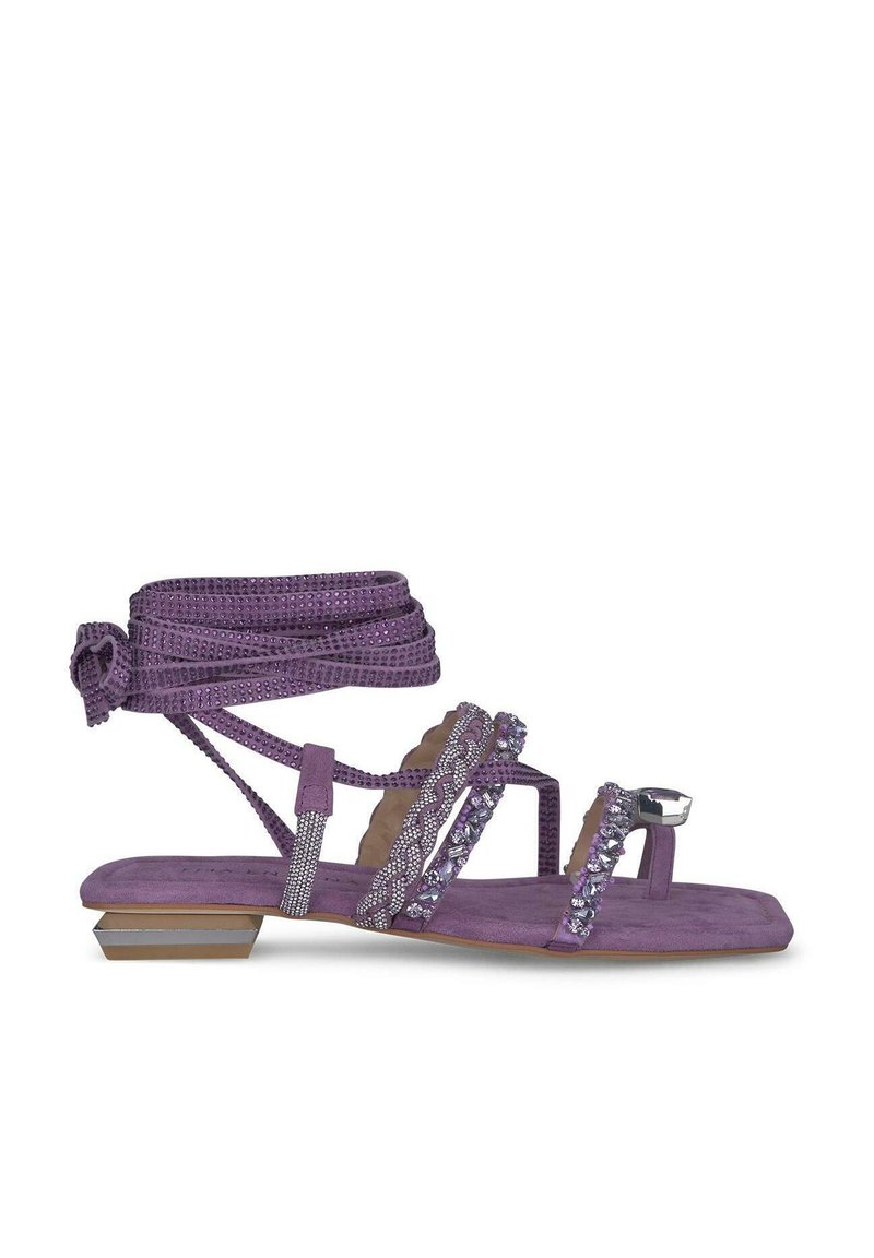 Sandalia de ante morado con tiras finas, adornada con cristales y una correa de tobillo anudada. Presenta un tacón bajo y una suela texturizada.