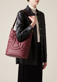 Burgundy leather shoulder bag with quilted pattern and gold-tone accents. Bag features a structured shape and adjustable strap.