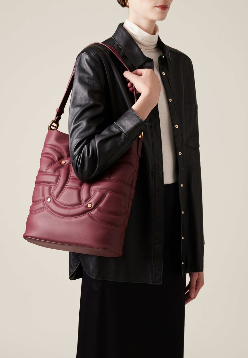 Burgundy leather shoulder bag with quilted pattern and gold-tone accents. Bag features a structured shape and adjustable strap.