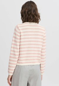 Rozā un baltā svītrainā džemperis ar teksturētu adījumu, garām piedurknēm un noapaļotu kakla izgriezumu, apvienots ar gaiši pelēkiem biksēm.