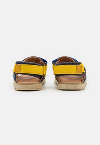 Sandaler med et design av gule og marineblå stropper, med en teksturert stoffoverdel og en lys brun gummisåle, som har justerbar borrelås lukking.