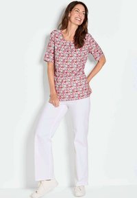Kurzärmliges Oberteil mit floralem Muster in Rosa und Weiß, kombiniert mit weißen geraden Hosen und hellen Sneakers.