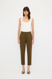Bílý top s čtvercovým výstřihem, který má vysoký pas, slim-fit nohavice v olivové zelené barvě a odpovídající lodičky s špičatou špičkou.