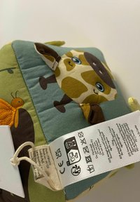 Jucărie de pluș din țesătură verde și albastră cu un design de girafă, cu accente marron, detalii brodate și o etichetă de îngrijire atașată.