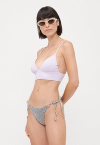 Haut de bikini lilas avec des fines bretelles, associé à un bas de bikini à carreaux noir et blanc avec des liens latéraux réglables.