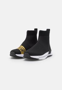 Svart stickade ankelskoter med vita sulor. Har gul logotyp på sidan. Design som är lätt att ta på sig med texturerad ovansida och dragflikar.