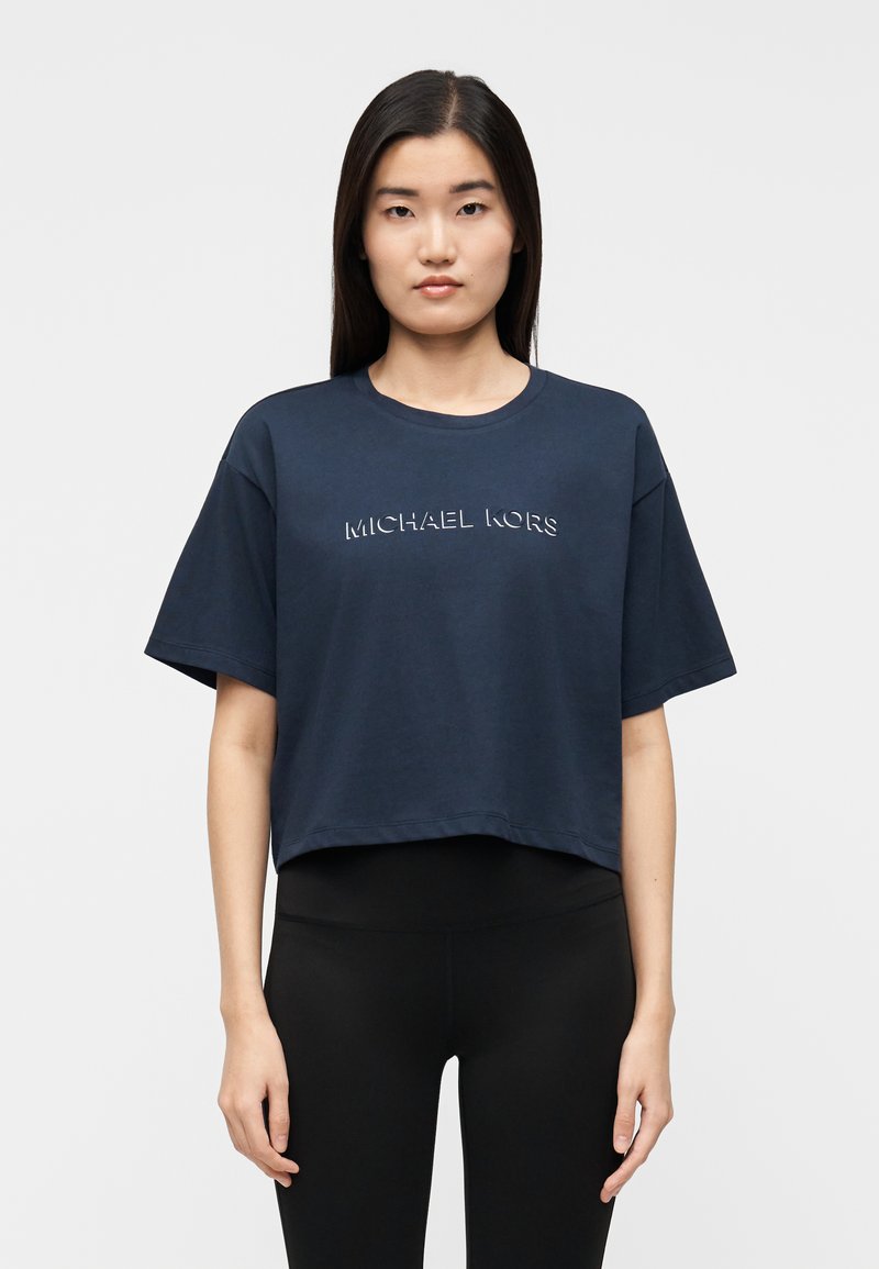 T-shirt corta azul marinho em algodão macio, com mangas curtas e decote arredondado. A frente exibe o logótipo "MICHAEL KORS" em relevo.