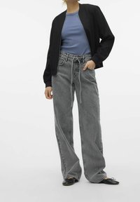 Grijze denim jeans met wijde pijpen, een hoge taille en een trekkoorddetail, gecombineerd met een blauw geribd topje en een zwarte bomberjack. Zwarte platte schoenen.