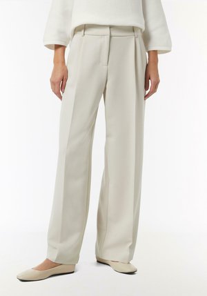 Weite Hose aus hellem beigen Stoff, mit hoher Taille, Falten und glatter Textur. Kombiniert mit passenden geschlossenen Ballerinas.
