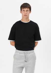 Black short-sleeve t-shirt with white collar and cuffs, paired with grey drawstring sweatpants, featuring a relaxed fit and soft fabric.