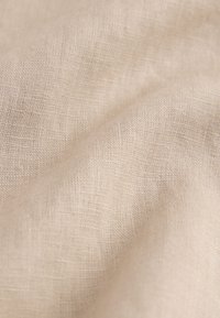 Hellbeige Leinenstoff mit einer strukturierten Webart, der weich fällt und subtile Farb- und Strukturvariationen zeigt.