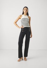 Svart og hvitstripet tank top med ribbestruktur, sammen med høyt liv svarte bukser med gullknapper, og beige blokk-hæl sandaler.