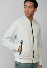 Witte bomberjack met een zwarte ritssluiting, geribbelde manchetten en zijzakken. Soepele textuur met een getailleerd ontwerp.