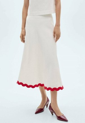 Falda de punto blanca con un dobladillo rojo en forma de onda, que cae por debajo de la rodilla. Combinada con tacones color burdeos, que presentan una punta afilada y un diseño de tacón curvado.