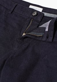 Ciemnoniebieskie spodnie o gładkiej fakturze, z zamkiem błyskawicznym i zapięciem na guzik, a także wewnętrznymi kieszeniami. Widoczna metka Esprit.