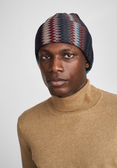 Căciulă tricotată cu un model în dungi multicolore, în roșu, albastru și gri. Material texturat, se fixează bine pe cap, cu un ușor efect de cădere în partea de sus.