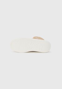 Baskets beige clair avec une tige texturée, dotées d'une semelle en caoutchouc crème rembourrée et de détails de marque subtils sur le côté.