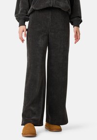 Leveled black corduroy pants with vertical ribbing, paired with tan slip-on shoes. The soft texture and relaxed fit provide comfort.
