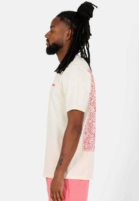 Roomkleurig T-shirt met korte mouwen, grote rode paisley-print op de achterkant, voorzien van een ronde hals en subtiele stikdetails.