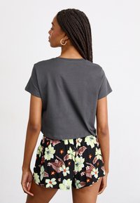 Gray cropped t-shirt with short sleeves, paired with black floral shorts featuring large green and brown flowers and contrasting orange accents.