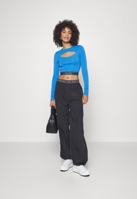 Blå langermet cropped topp med en utskjæring, kombinert med svarte løse bukser og hvite sneakers, fullført med en svart håndveske.