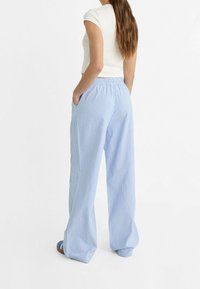 Pantalons larges rayés bleu clair avec une taille élastique et des poches latérales. Le tissu a une texture lisse. Pas de motifs ou d'accents visibles.