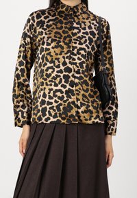 Leopardenmuster Hemd mit Knöpfen, das eine weiche Textur, lange Ärmel und einen klassischen Kragen bietet, kombiniert mit einem dunklen Faltenrock und einer kleinen Tasche.