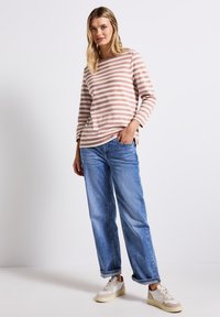 Lange mouwen, ronde hals top in lichtroze met witte strepen, gecombineerd met losse blauwe denim jeans en crèmekleurige sneakers met beige accenten.