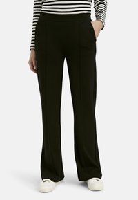 Schwarze, weit geschnittene Hose mit glatter Textur, seitlichen Taschen und hohem Bund. Tragen mit einem gestreiften Langarmoberteil.