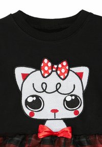 Schwarzer Pullover mit einem Katzenmotiv, das weißes Fell, große Augen, eine rote gepunktete Schleife und einen schwarz-roten karierten Rock zeigt.