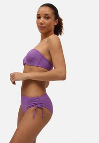 Top de bikini sin tirantes de color púrpura con una textura suave, combinado con braguitas de bikini de cintura alta que presentan un detalle de lado fruncido y lazos.