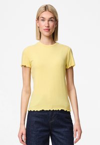 Dzeltena ribota īsām piedurknēm topa ar noapaļotu kakla izgriezumu un viļņotām malām, apvienots ar tumši zilām denima biksēm. Gluda tekstūra, pieguļoša forma.