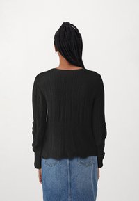 Zwarte gebreide trui met geribbelde textuur, lange mouwen en een ronde zoom, gecombineerd met een blauwe denimrok. Achteraanzicht getoond.